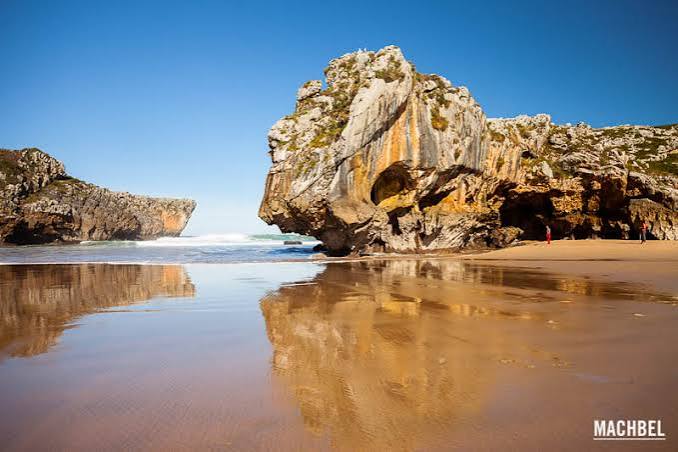 Playa de Cuevas del Mar en Llanes Asturias con roca característica arena dorada y cielo azul reflejado