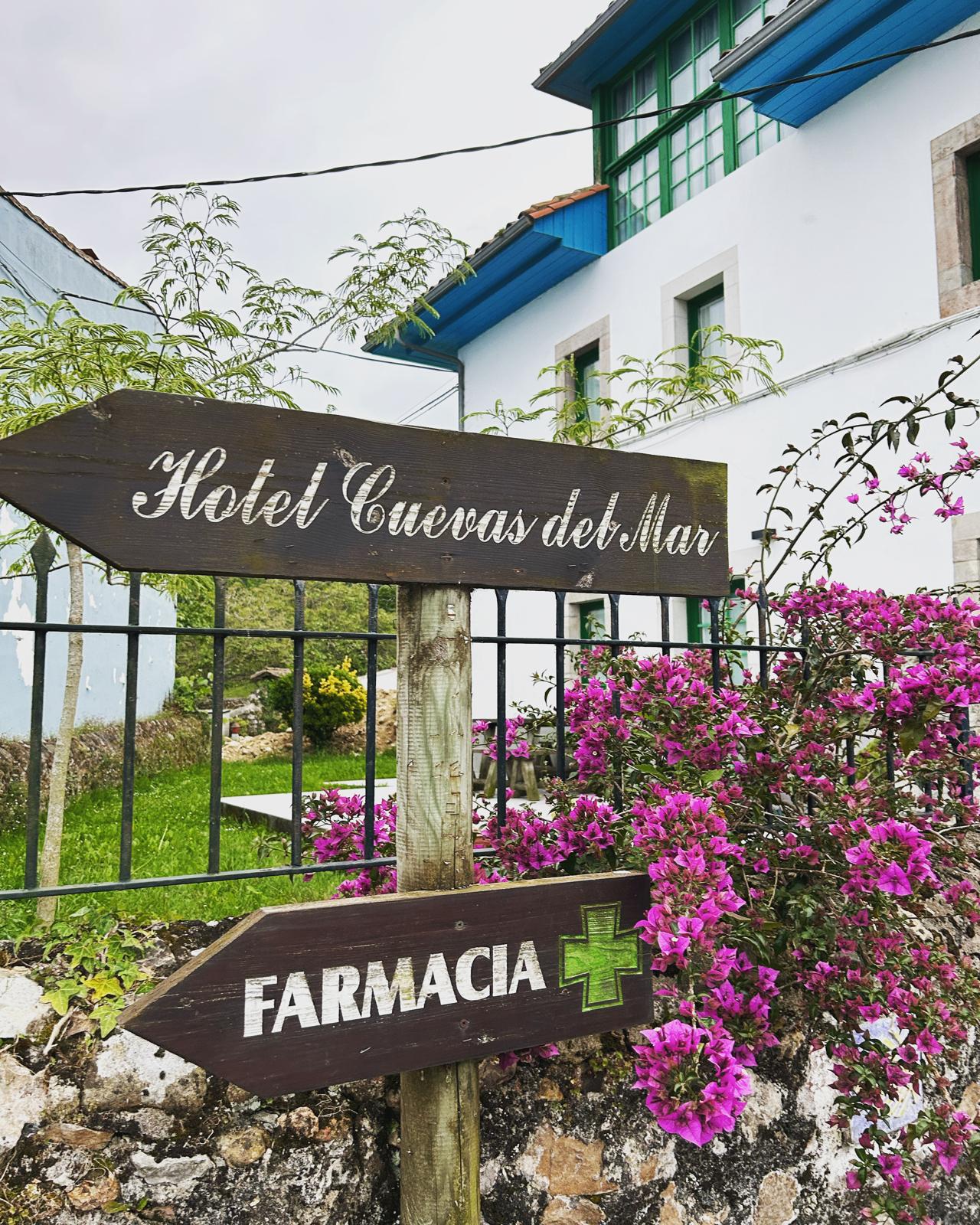 Señal de madera Hotel Cuevas del Mar con flores y fachada al fondo en Nueva de Llanes Asturias